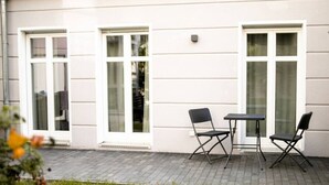 Ein Sitzbereich im Freien mit zwei Stühlen und einem Tisch, direkt neben einem Gebäude mit großen Fenstern.