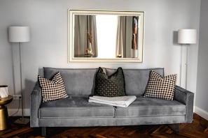 A grey sofa with patterned cushions, a large mirror above, and two floor lamps on either side.