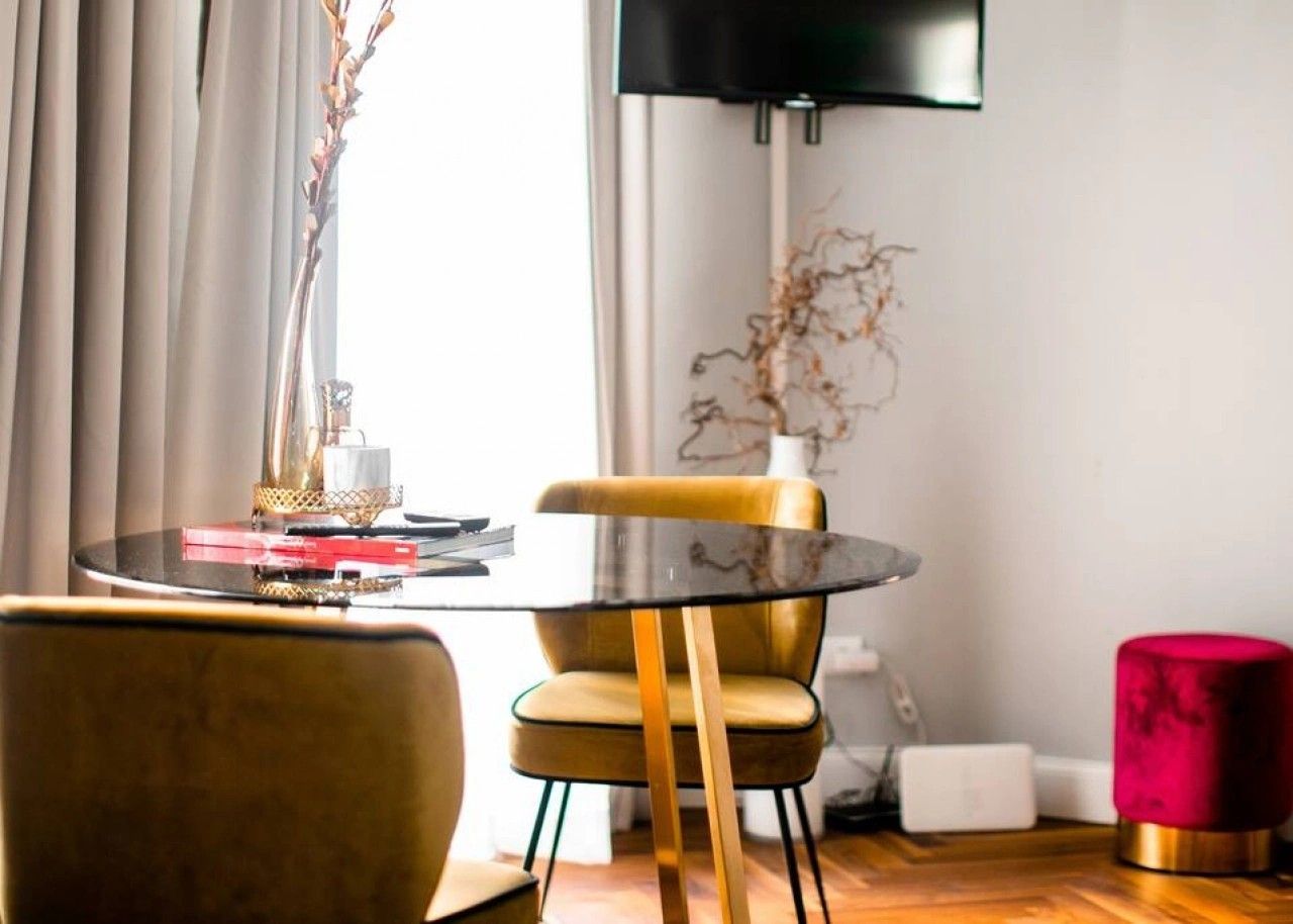 Una sala de estar moderna con una mesa redonda de vidrio, una butaca amarilla, un reposapiés rojo y un televisor de pantalla plana montado en la pared.