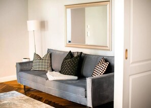 A grey sofa with patterned cushions, a white throw blanket, and a mirror with a gold frame on the wall. - Arbio I Renovated Studio in Charlottenburg (Berlin)