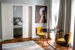 A modern hotel room with a bed, a round table with chairs, a painting on the wall, and a view through an open door. - Arbio I Renovated Studio in Charlottenburg (Berlin)