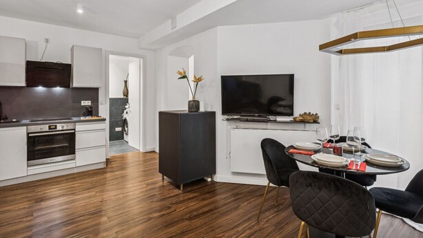 A modern kitchen with a built-in oven, a dining area with a round table and black chairs, and a flat-screen TV mounted above the table. - Arbio I New renovated Apart Schöneberg S-Bahn (Berlin)