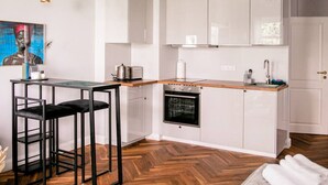 A modern kitchen with white cabinets, a wooden countertop, a built-in oven, and a small dining area with a black metal table and chairs. - Arbio I Cozy Apart in Charlottenburg (Berlin)