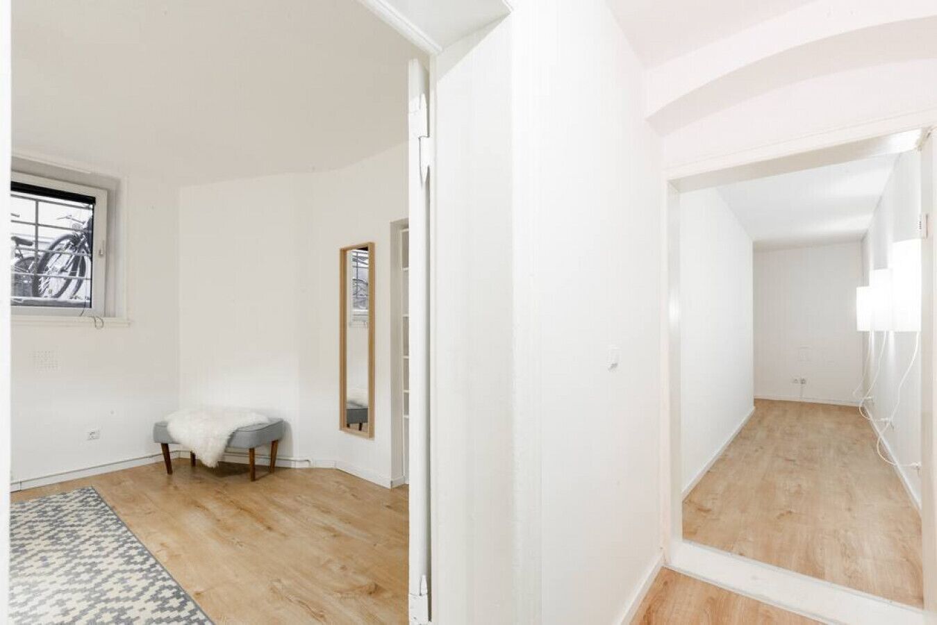 Ein Zimmer mit Holzboden, einem grauen Stuhl, einem kleinen Tisch und einem Spiegel an der Wand.