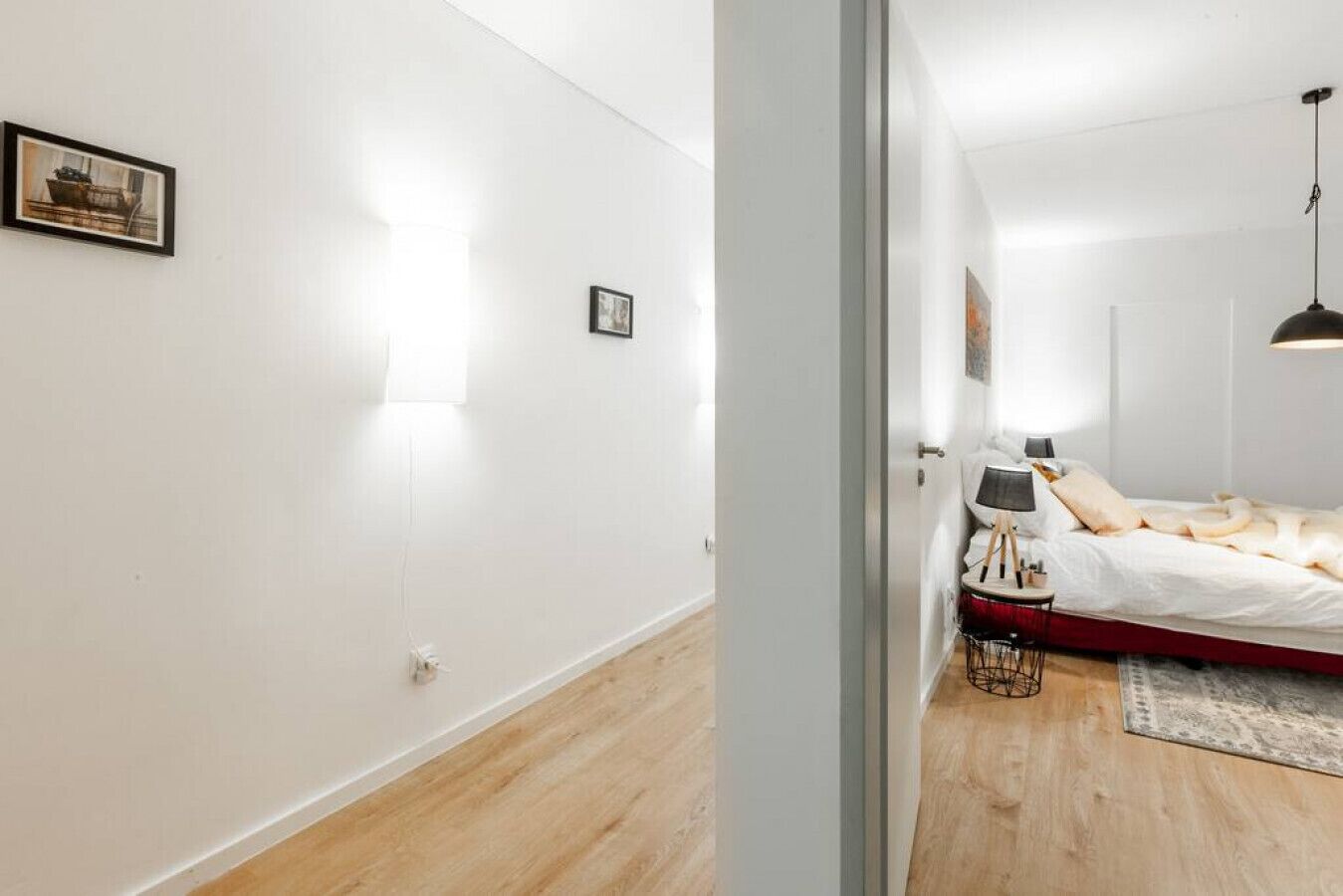 A modern bedroom with a bed, bedside table, lamp, and a small chair.