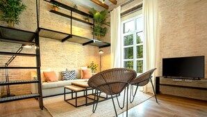Un salon moderne comprenant un canapé, deux fauteuils en osier, une table basse, un téléviseur et un escalier agrémenté de plantes.