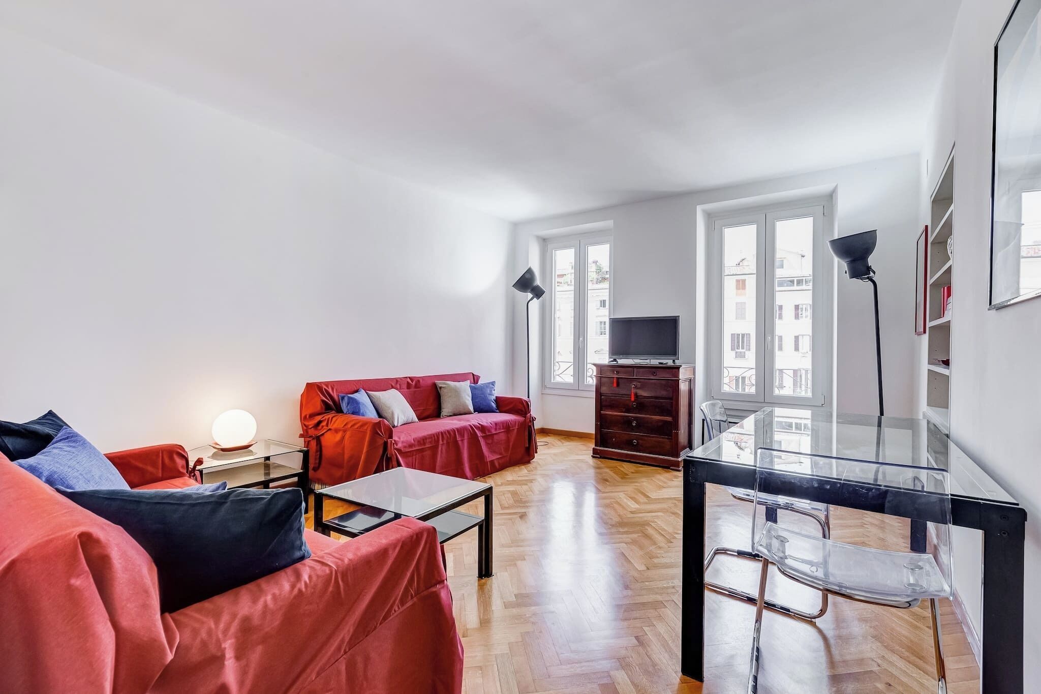 A modern living room with a red sofa, a glass coffee table, and a TV on a wooden cabinet.