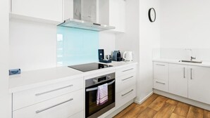 A modern kitchen with white cabinetry, a built-in oven, a stainless steel range hood, and a coffee maker.