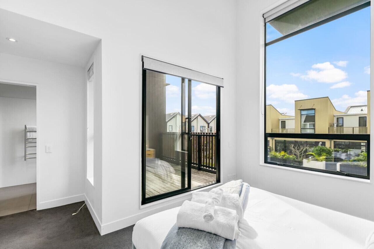 A modern bedroom with a large window, a sliding door, and a view of neighboring buildings.