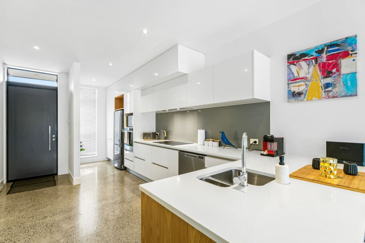 A modern kitchen with white cabinetry, a stainless steel sink, and a coffee machine.