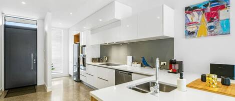A modern kitchen with white cabinetry, a stainless steel sink, and a coffee machine.
