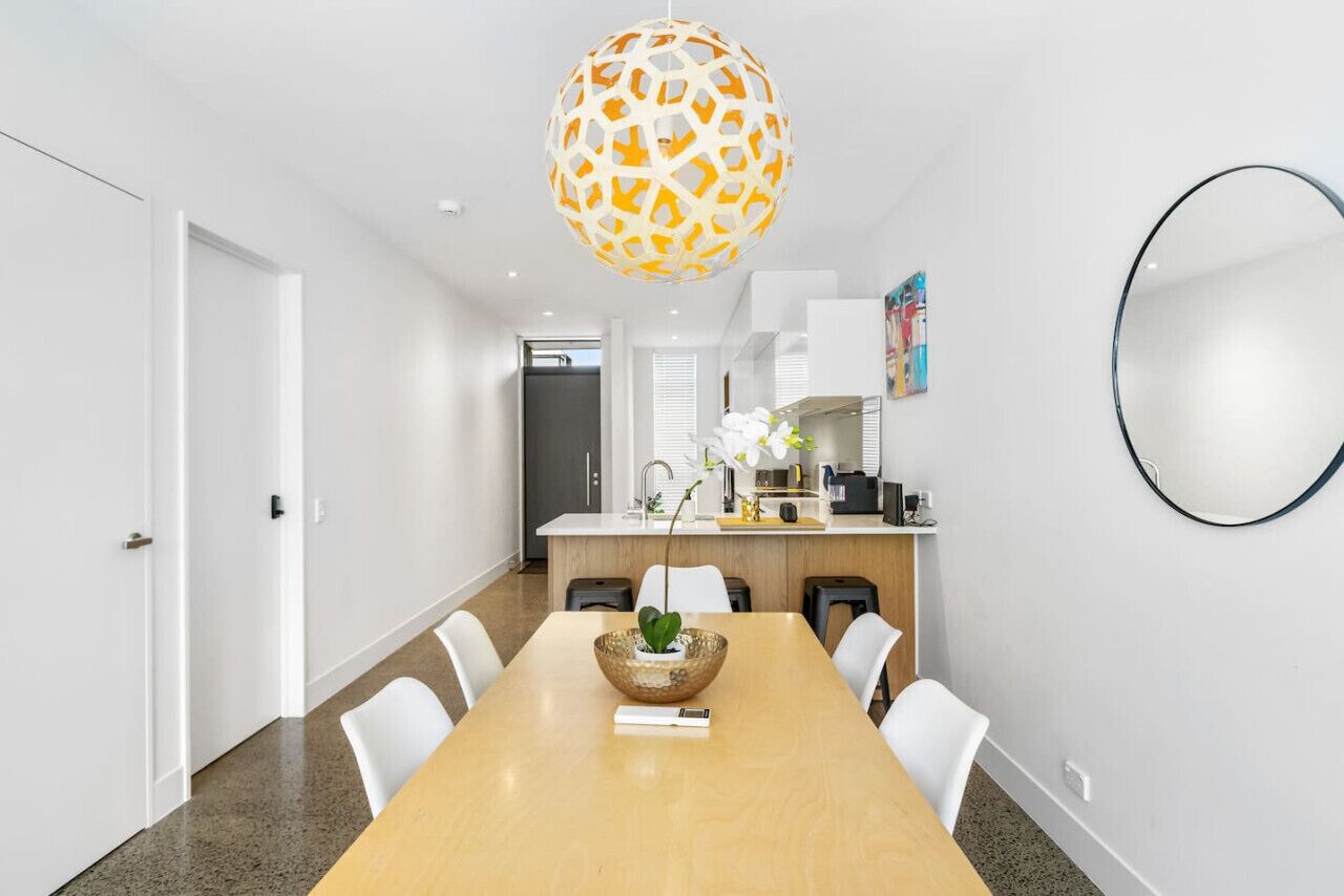 Un moderno comedor con una mesa de madera, sillas blancas, un cuenco decorativo con una planta y una lámpara esférica original.