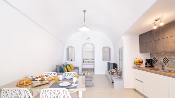 Une cuisine moderne avec un coin repas, des murs blancs et une arche centrale qui mène à une chambre.