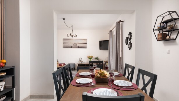 Un coin repas avec une table en bois dressée pour six personnes, des chaises noires et un lustre.