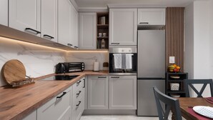 Une cuisine moderne avec des armoires blanches, un plan de travail en bois, un four encastré et un coin repas comprenant une table et des chaises.