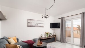 Un salon moderne avec un canapé gris, une table basse, un téléviseur à écran plat et une porte-fenêtre coulissante donnant sur l’extérieur.