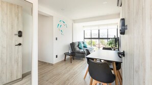 A modern living room with a dining area, a grey sofa, a small table, and a large window with a view. - Departamento Astoria (Acapulco de Juarez)