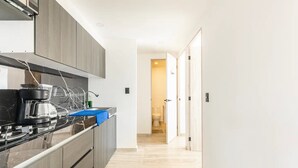 A narrow kitchen with dark cabinets, a black countertop, and a coffee maker. A blue towel is on the counter. - Departamento Astoria (Acapulco de Juarez)