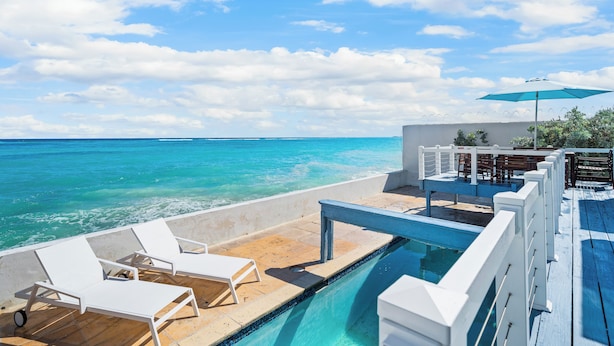A poolside area with lounge chairs, a pool, and a view of the ocean.