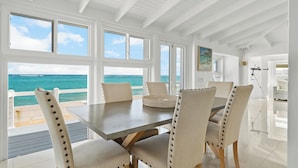 A dining area with a view of the ocean, white walls, and a ceiling with exposed beams.