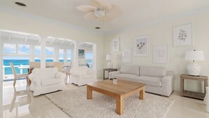 A spacious living room with a large window overlooking the ocean, a white sofa, a wooden coffee table, and a ceiling fan.