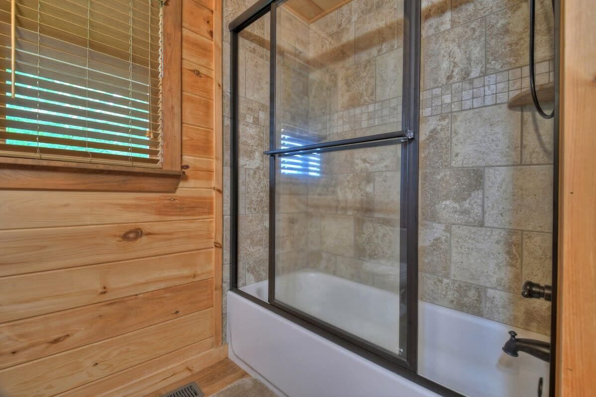 A wooden cabin bathroom with a glass-enclosed shower and a white bathtub.