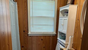 A bathroom with wooden walls, a toilet, a sink, a window with blinds, and a shower curtain. - Peaceful Farm Getaway (Mullins)