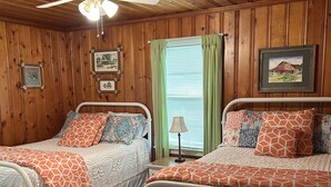 A room with two beds, wooden paneling, a ceiling fan, framed pictures, and a window with curtains. - Peaceful Farm Getaway (Mullins)