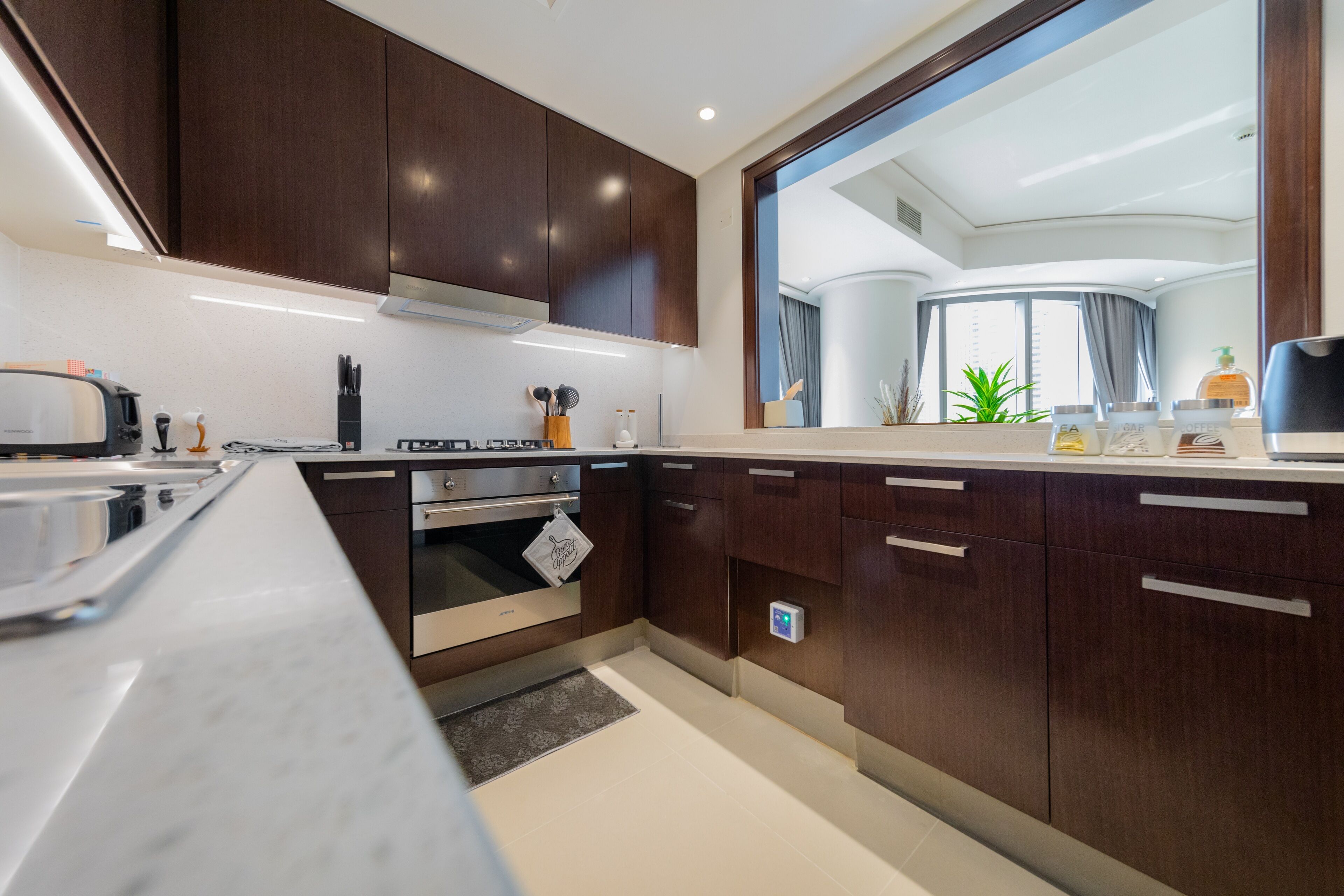 A modern kitchen with dark wood cabinets, stainless steel appliances, and a large window offering a view of the interior.