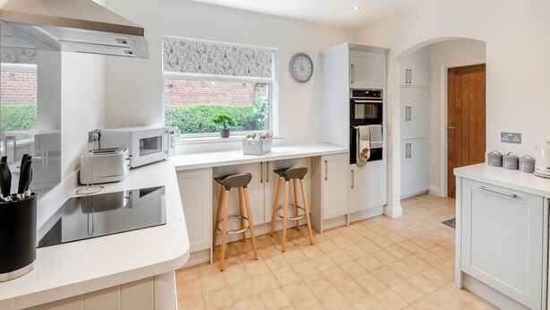 Een moderne keuken met witte kastjes, een inbouwoven, een magnetron en een raam met uitzicht op groen.