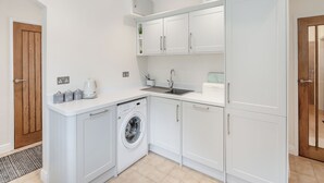 Een compacte keuken met witte kastjes, een inbouw wasmachine, een spoelbak en een klein aanrecht met een koffiezetapparaat.