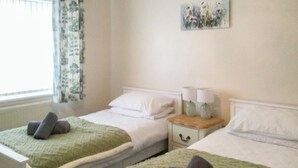 Een hotelkamer met twee bedden, elk met een groene deken en opgerolde handdoeken. Er staat een nachtkastje met twee lampen en er hangt een schilderij aan de muur.