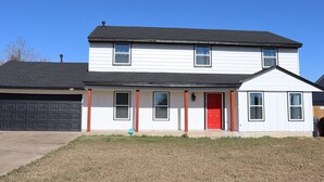 A two-story house with a red door, white siding, and a garage. - Chisholm Creek by Top golf 3 (Oklahoma City)