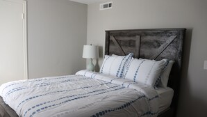 A neatly made bed with a white and blue patterned bedspread, a wooden headboard, and a bedside table with a lamp. - Chisholm Creek by Top golf 3 (Oklahoma City)