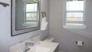 A bathroom with a large mirror, a sink, a toilet, and a window with blinds. - Chisholm Creek by Top golf 3 (Oklahoma City)