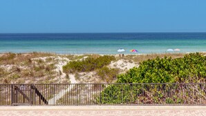 A beach view with a clear sky, a sandy path leading to the water, and a fence in the foreground.