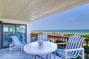 A balcony with two striped lounge chairs, a round table with a vase, and a view of the beach and ocean. - Indian Rocks Beachfront Condo-steps to sand & restaurants/shopping, 2 pkg spots  (Indian Rocks Beach)