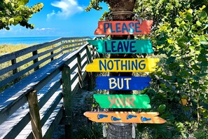 A wooden signpost with colorful signs against a backdrop of a wooden walkway and a clear blue sky.