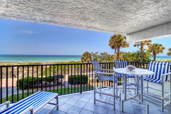 A balcony with a view of the ocean, featuring striped chairs and a small table.