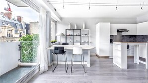 A modern kitchen with white cabinets, a dining area with a white table and chairs, and a view of the city through large windows. - Muette - Lamartine 1bdr by B'Your Home (Paris)