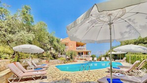 A poolside area with lounge chairs, umbrellas, and a stone-tiled pool.
