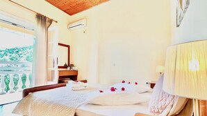 A bedroom with a bed, bedside table, lamp, and a window with a view of greenery.