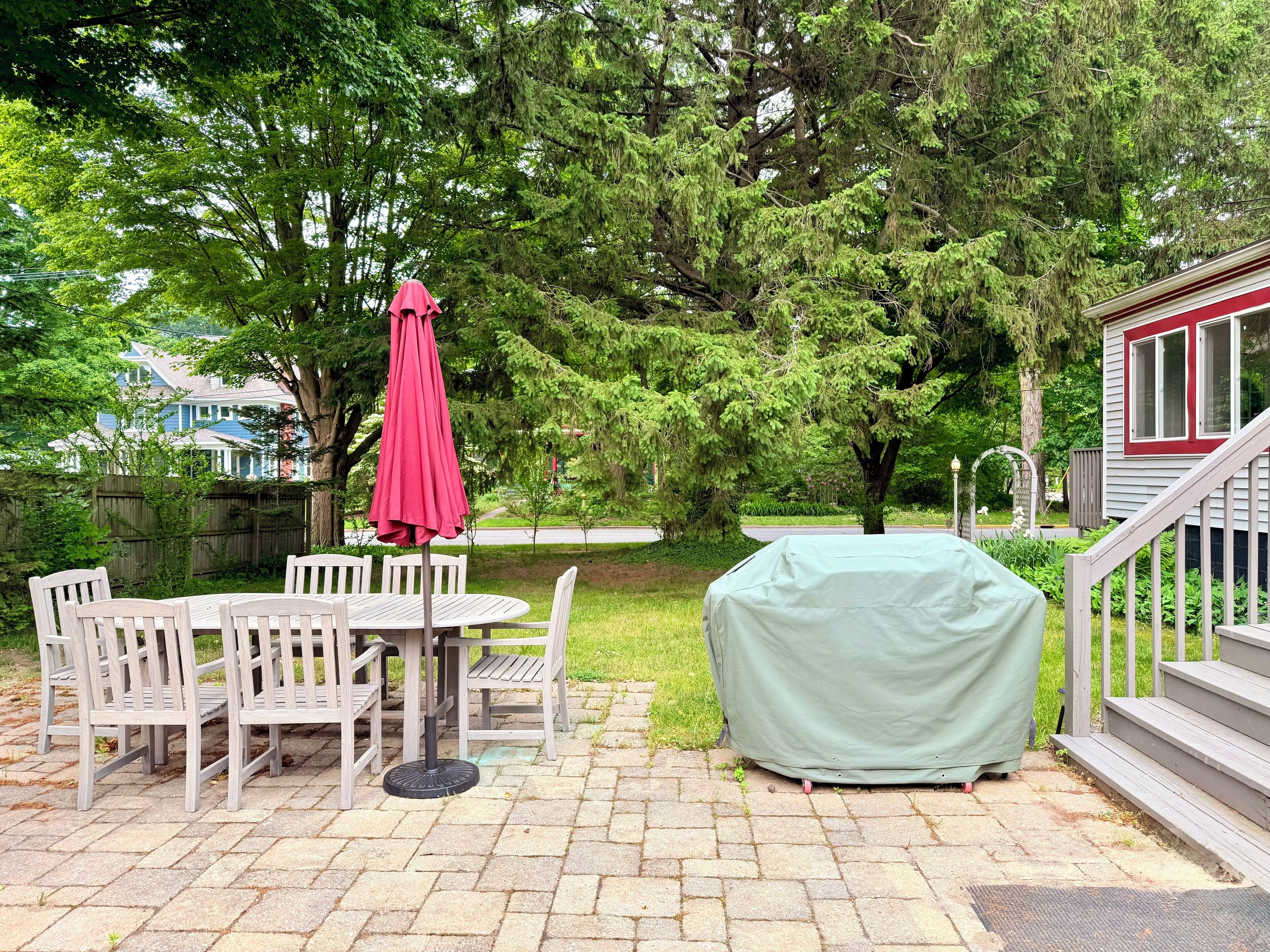 A patio with a covered grill, a table with chairs, and a red umbrella.