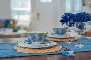 Una mesa de comedor con manteles individuales azules, un mantel individual tejido y un sujetapapeles azul con servilletas dobladas.