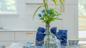A dining table set with blue napkins, clear glassware, and a vase with green foliage and blue flowers. - Levy inn Luxury cottage (San Antonio)