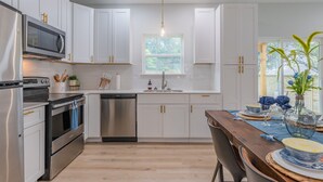 A modern kitchen with white cabinets, stainless steel appliances, and a wooden dining table set for six. - Levy inn Luxury cottage (San Antonio)