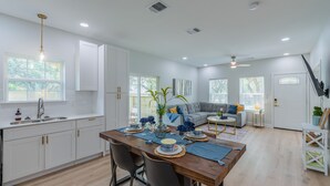 A modern kitchen with white cabinets, a wooden dining table, and a gray sofa in the living area. - Levy inn Luxury cottage (San Antonio)