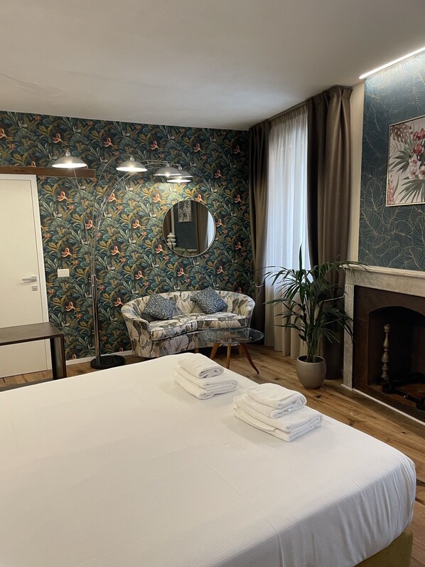 A hotel room with a bed, a sofa, a mirror, a fireplace, and a potted plant.