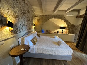 A bedroom with a stone wall, a bed with white bedding, a bedside table with a phone, and a wall-mounted lamp. - La Bartolomea Home&Suite (Pitigliano)