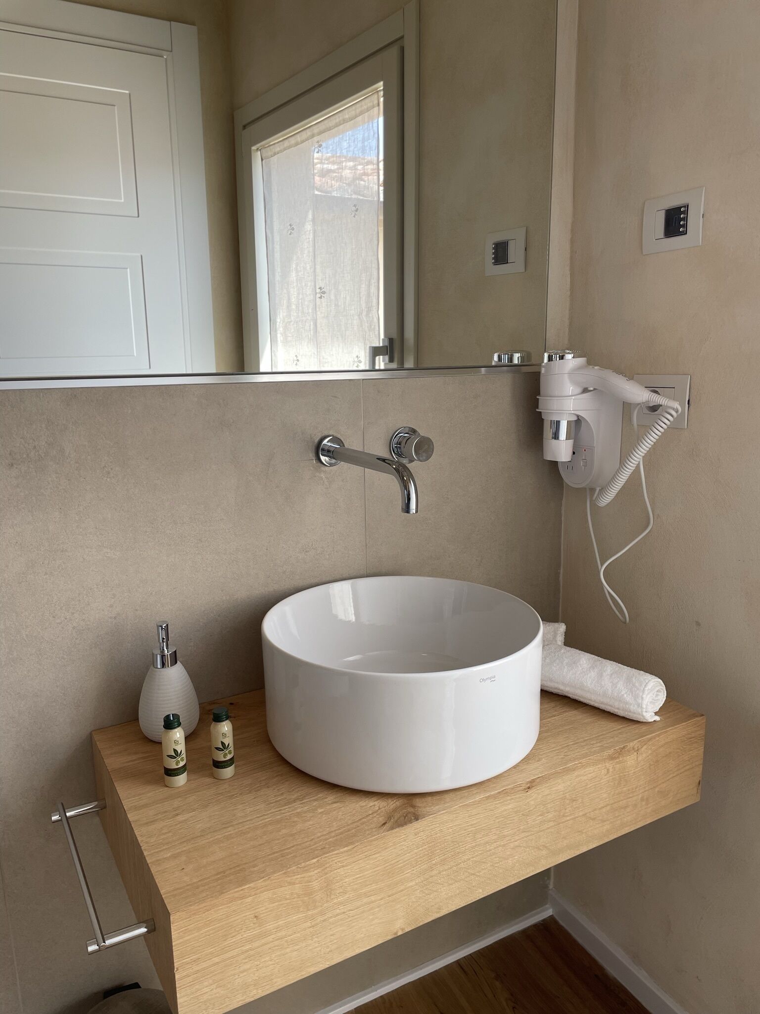 A bathroom with a round white sink, a mirror, a hairdryer, and two small bottles on the counter.
